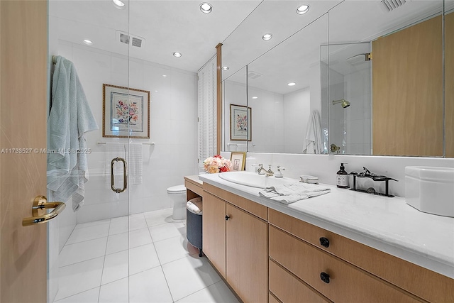 bathroom featuring tile walls, vanity, toilet, a shower with door, and tile patterned floors