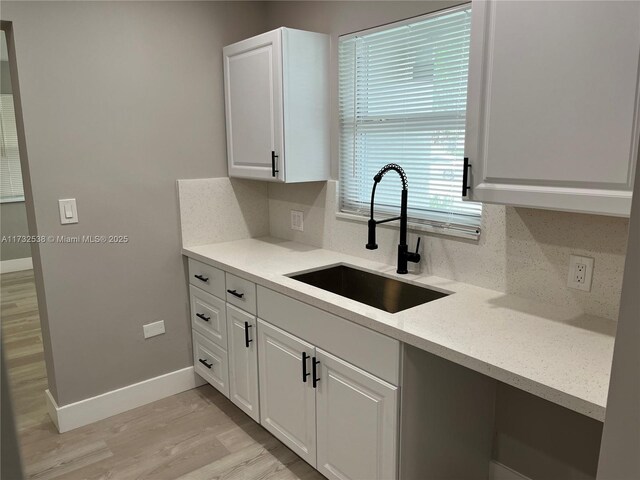 kitchen with tasteful backsplash, sink, light hardwood / wood-style flooring, and white cabinets