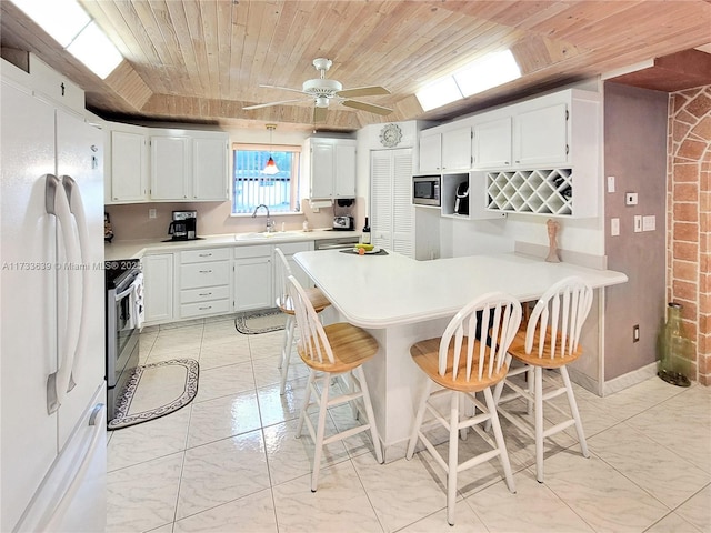 kitchen featuring sink, white cabinets, a kitchen breakfast bar, stainless steel appliances, and wooden ceiling