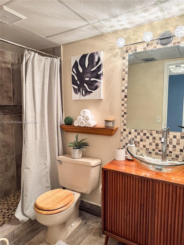 full bath with a tile shower, toilet, visible vents, and backsplash