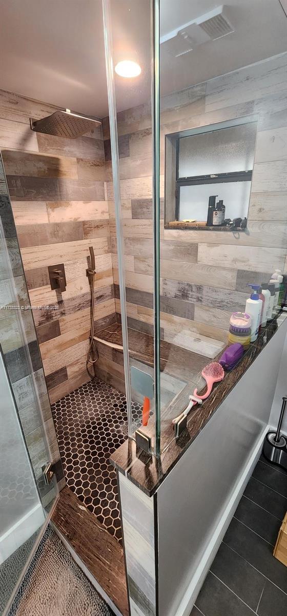 bathroom with tile patterned floors, a tile shower, and wood walls