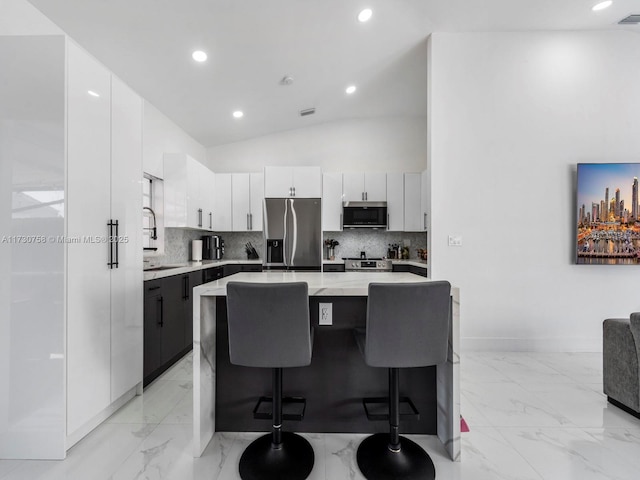 kitchen with vaulted ceiling, a kitchen island, white cabinetry, a kitchen breakfast bar, and stainless steel appliances