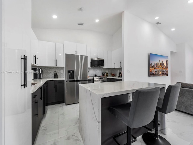 kitchen with a kitchen island, white cabinetry, appliances with stainless steel finishes, and lofted ceiling