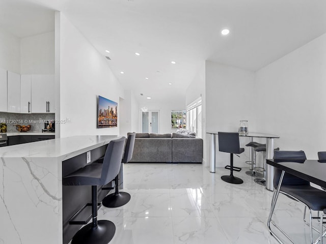 interior space featuring lofted ceiling, a breakfast bar area, white cabinetry, tasteful backsplash, and light stone countertops