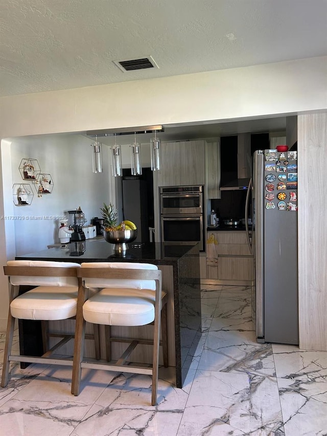 kitchen featuring wall chimney range hood, stainless steel appliances, a kitchen breakfast bar, and kitchen peninsula