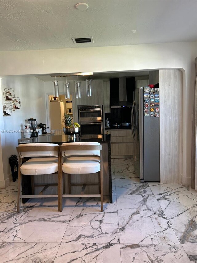 kitchen featuring a kitchen bar, wall chimney exhaust hood, and appliances with stainless steel finishes