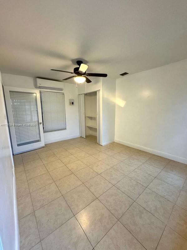 spare room featuring ceiling fan, a wall mounted AC, and light tile patterned floors