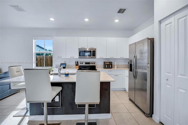 kitchen with light tile patterned flooring, white cabinetry, a kitchen breakfast bar, an island with sink, and stainless steel appliances