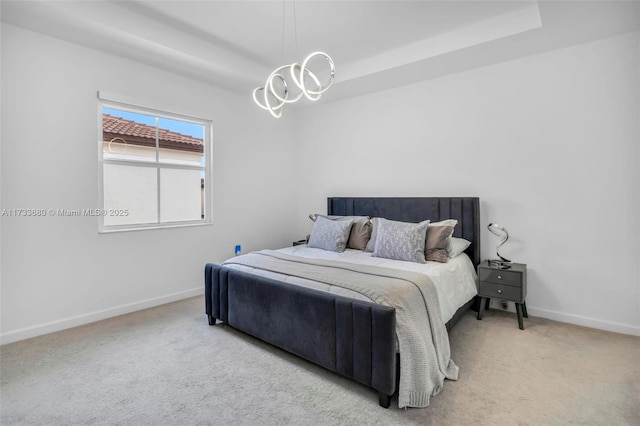 carpeted bedroom with a tray ceiling and a chandelier