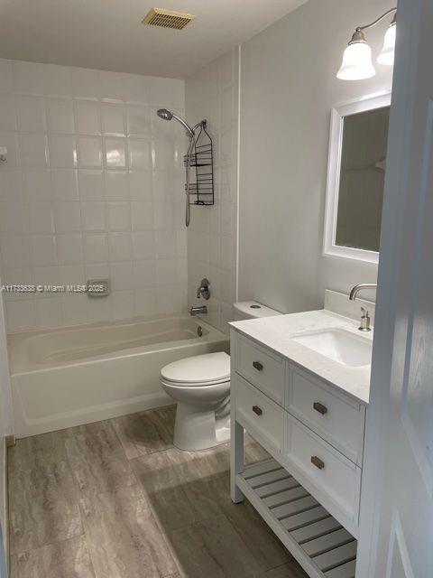 full bathroom featuring hardwood / wood-style flooring, vanity, toilet, and tiled shower / bath