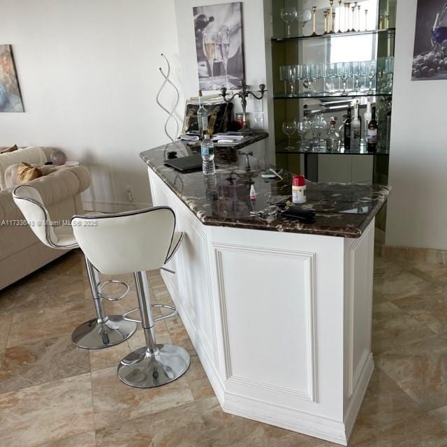 bar with dark stone countertops and white cabinets