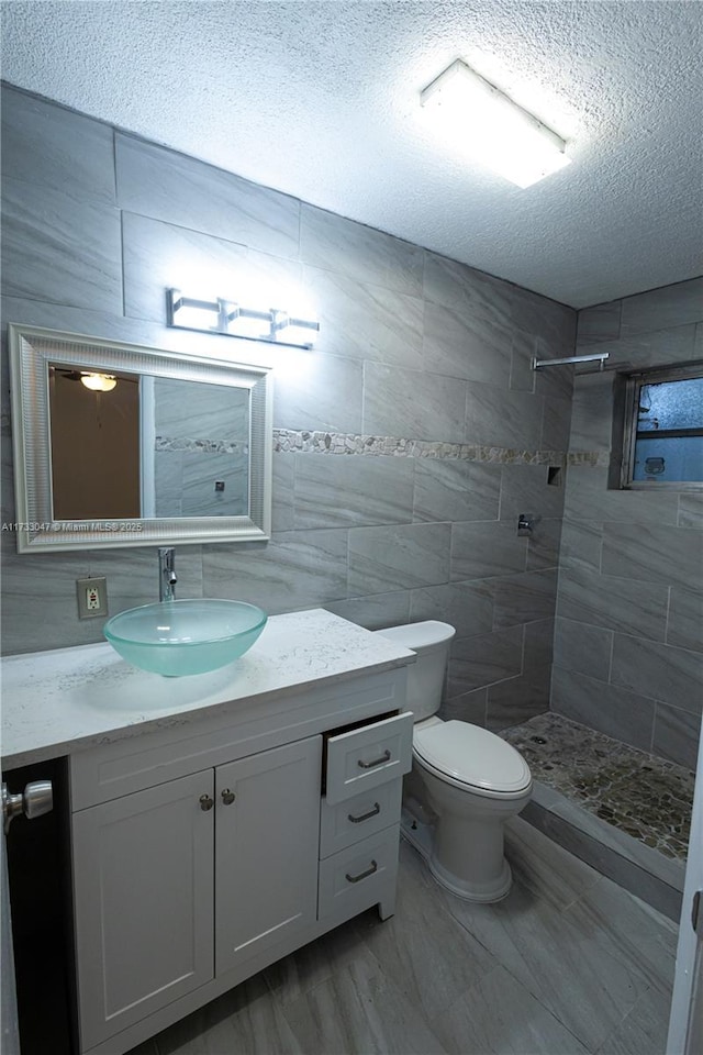 bathroom with a tile shower, tile walls, vanity, toilet, and a textured ceiling