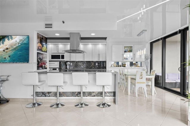 19667 Turnberry Way Unit 20B, Aventura, FL 33180 - kitchen with island range hood, stainless steel microwave, a breakfast bar, decorative backsplash, and white cabinetry