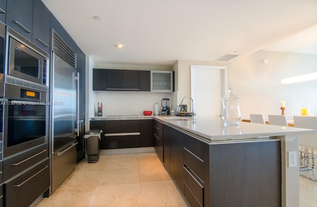 kitchen featuring sink, a breakfast bar, built in appliances, and kitchen peninsula