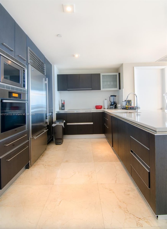 kitchen with sink, built in appliances, dark brown cabinetry, and kitchen peninsula