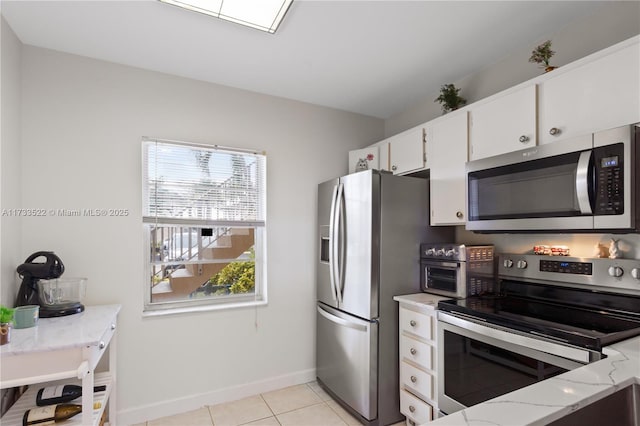 kitchen with light tile patterned floors, baseboards, appliances with stainless steel finishes, light stone countertops, and white cabinetry