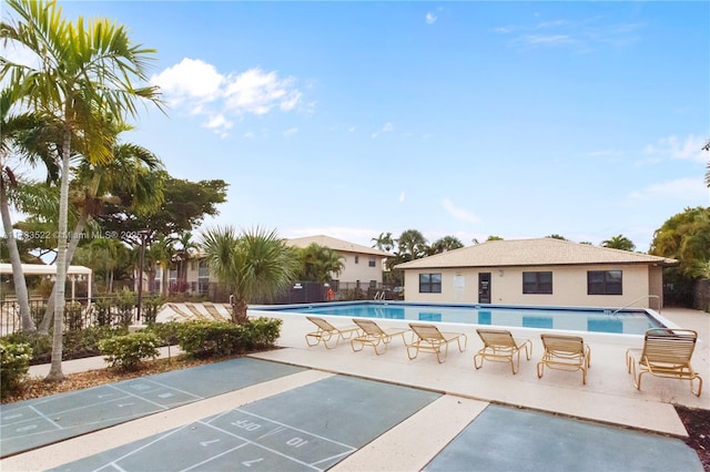 exterior space featuring shuffleboard, a patio area, fence, and a pool