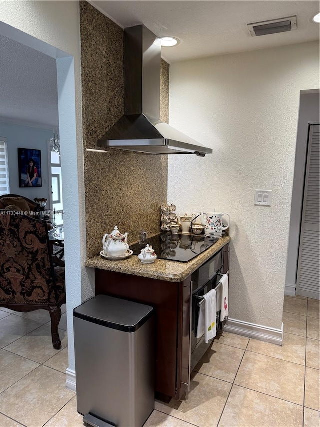 kitchen with dark brown cabinetry, stone countertops, light tile patterned floors, wall chimney range hood, and black appliances