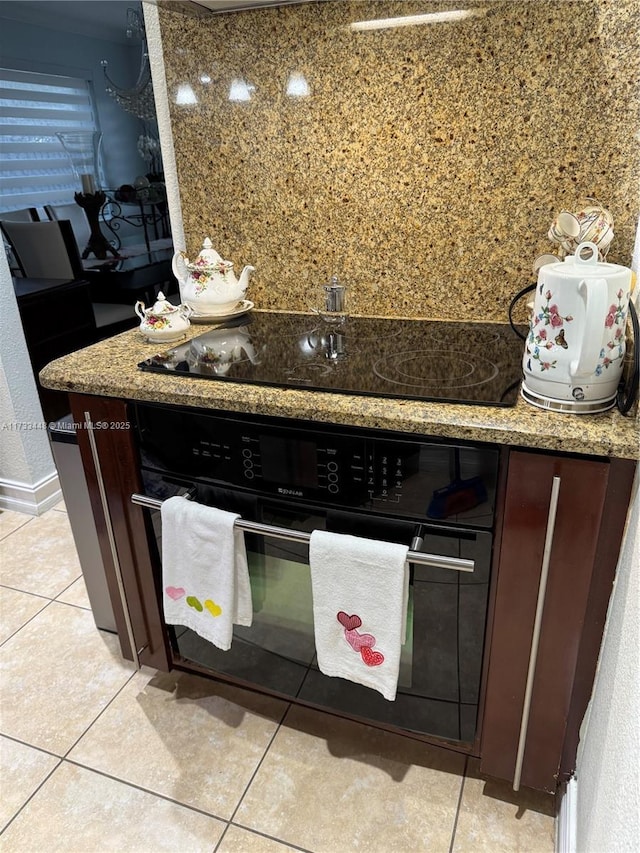 kitchen featuring stone countertops, light tile patterned floors, dark brown cabinets, and black appliances