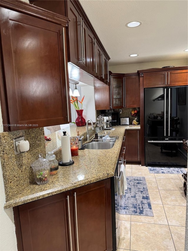 kitchen with black fridge, sink, light stone counters, and light tile patterned floors