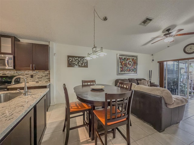 dining space featuring light tile patterned flooring, lofted ceiling, sink, a textured ceiling, and ceiling fan