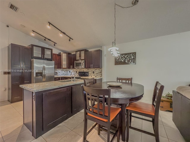 kitchen featuring vaulted ceiling, light tile patterned flooring, dark brown cabinetry, stainless steel appliances, and a center island with sink