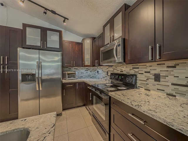 kitchen featuring tasteful backsplash, lofted ceiling, light tile patterned floors, light stone counters, and stainless steel appliances