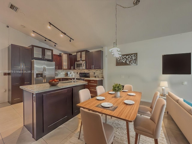 kitchen with light tile patterned flooring, appliances with stainless steel finishes, a kitchen island with sink, and decorative backsplash