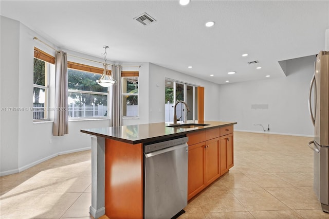 kitchen with light tile patterned flooring, appliances with stainless steel finishes, decorative light fixtures, sink, and a kitchen island with sink