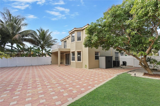 rear view of house with a balcony, a yard, central AC unit, and a patio