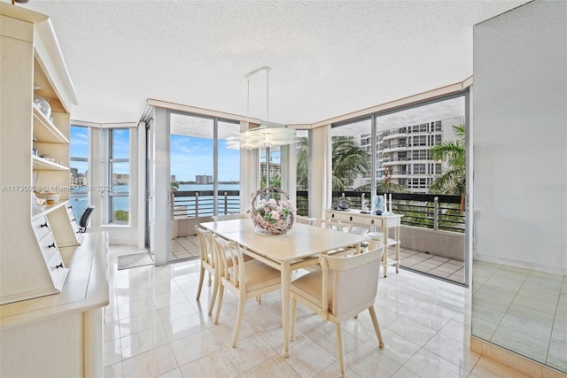 tiled dining space featuring a water view, a textured ceiling, and a wall of windows