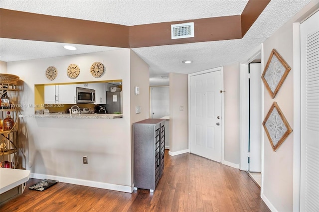 kitchen featuring white cabinetry, light stone counters, stainless steel appliances, dark wood-type flooring, and a textured ceiling