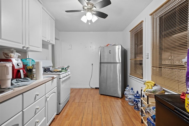 kitchen with gas stove, light wood-type flooring, stainless steel fridge, ceiling fan, and white cabinets