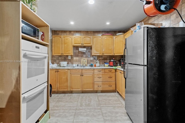 kitchen with sink, stainless steel refrigerator, double oven, light stone countertops, and decorative backsplash