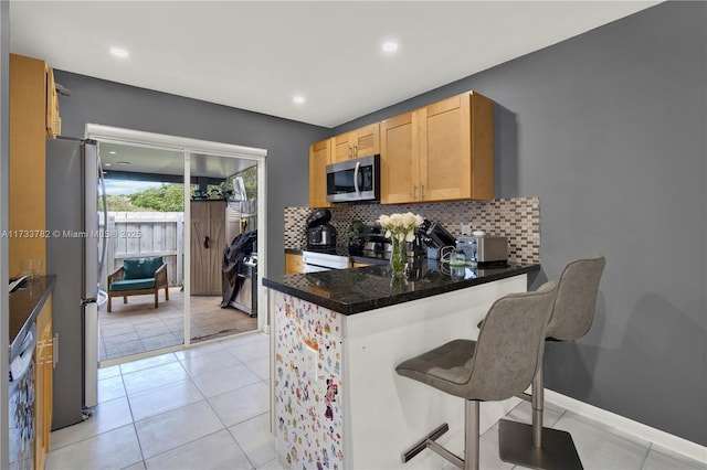 kitchen with light tile patterned floors, a breakfast bar, appliances with stainless steel finishes, tasteful backsplash, and kitchen peninsula