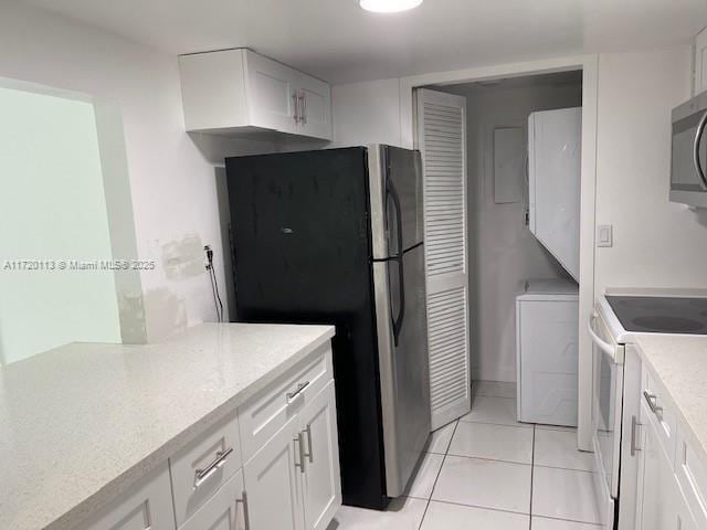 kitchen with light tile patterned floors, white electric stove, white cabinets, and refrigerator