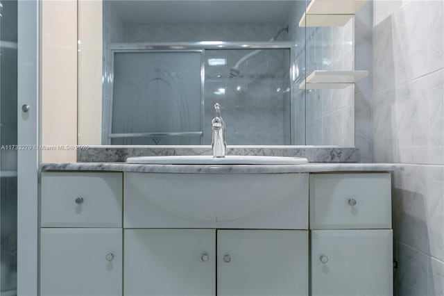 bathroom featuring a shower with door, vanity, and tile walls