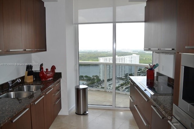 kitchen featuring sink, light tile patterned floors, dark stone counters, and a healthy amount of sunlight