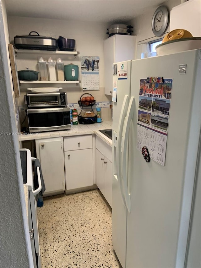 kitchen with white cabinetry, range, white refrigerator with ice dispenser, and tile countertops