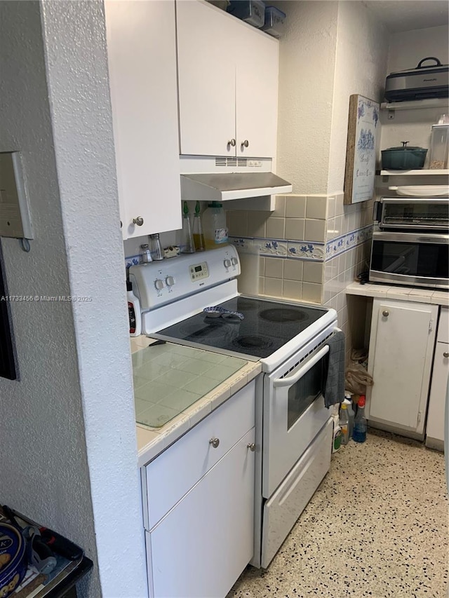 kitchen featuring tile counters, tile walls, white cabinets, and electric range