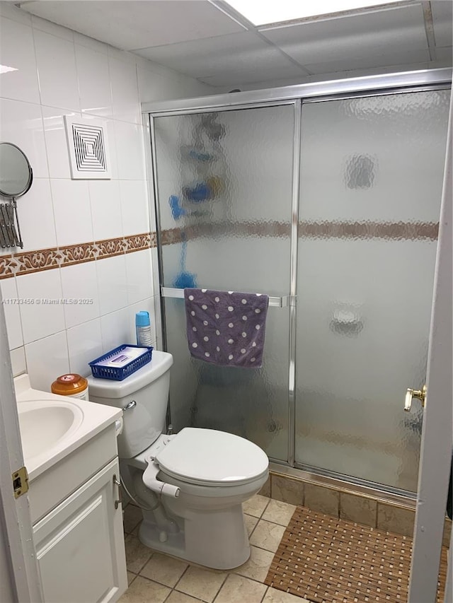 bathroom with toilet, a shower with shower door, tile walls, vanity, and tile patterned flooring