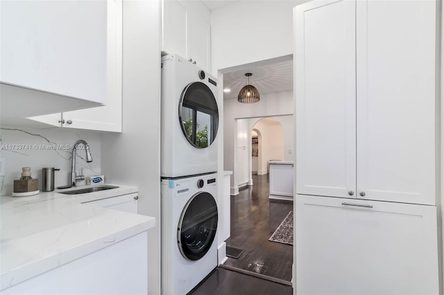 laundry room with stacked washer / dryer, dark hardwood / wood-style flooring, sink, and cabinets