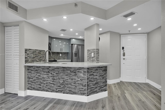 kitchen with sink, white cabinetry, stainless steel refrigerator with ice dispenser, light hardwood / wood-style floors, and kitchen peninsula