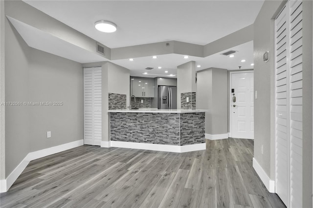 kitchen with white cabinetry, sink, stainless steel fridge, light hardwood / wood-style floors, and kitchen peninsula