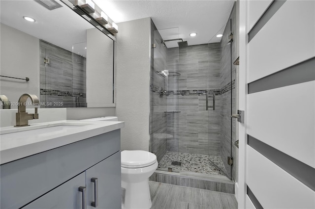 bathroom featuring vanity, a textured ceiling, a shower with door, and toilet