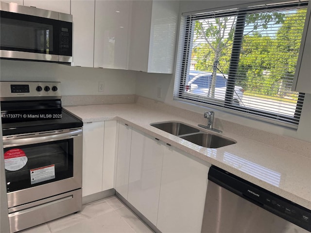 kitchen with sink, appliances with stainless steel finishes, light stone counters, white cabinets, and light tile patterned flooring