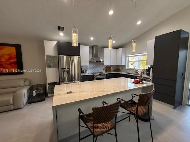 kitchen featuring a breakfast bar area, a center island, light stone counters, stainless steel appliances, and wall chimney range hood