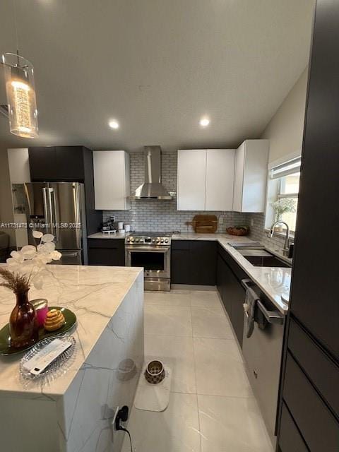 kitchen with wall chimney range hood, sink, hanging light fixtures, stainless steel appliances, and white cabinets