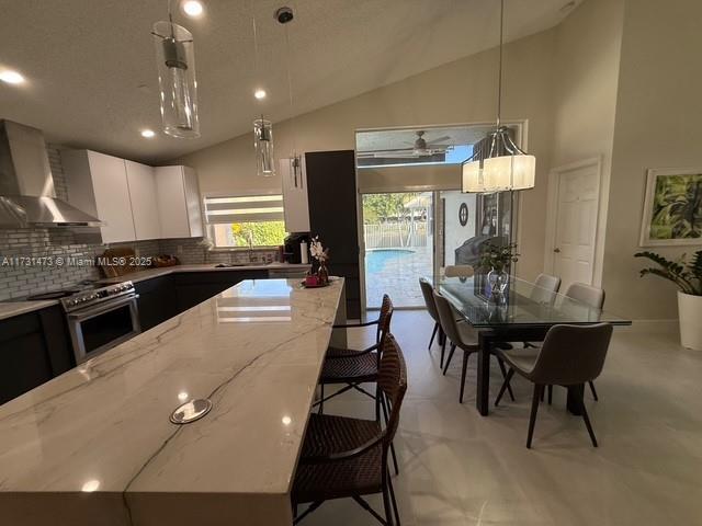 kitchen with white cabinetry, wall chimney exhaust hood, stainless steel gas range, and hanging light fixtures