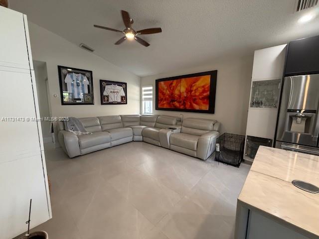 living room featuring a textured ceiling, vaulted ceiling, and ceiling fan